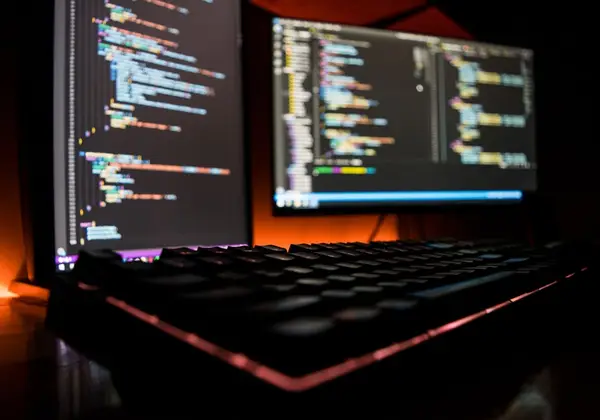 A desk with a monitor, keyboard and phone under coloured light
